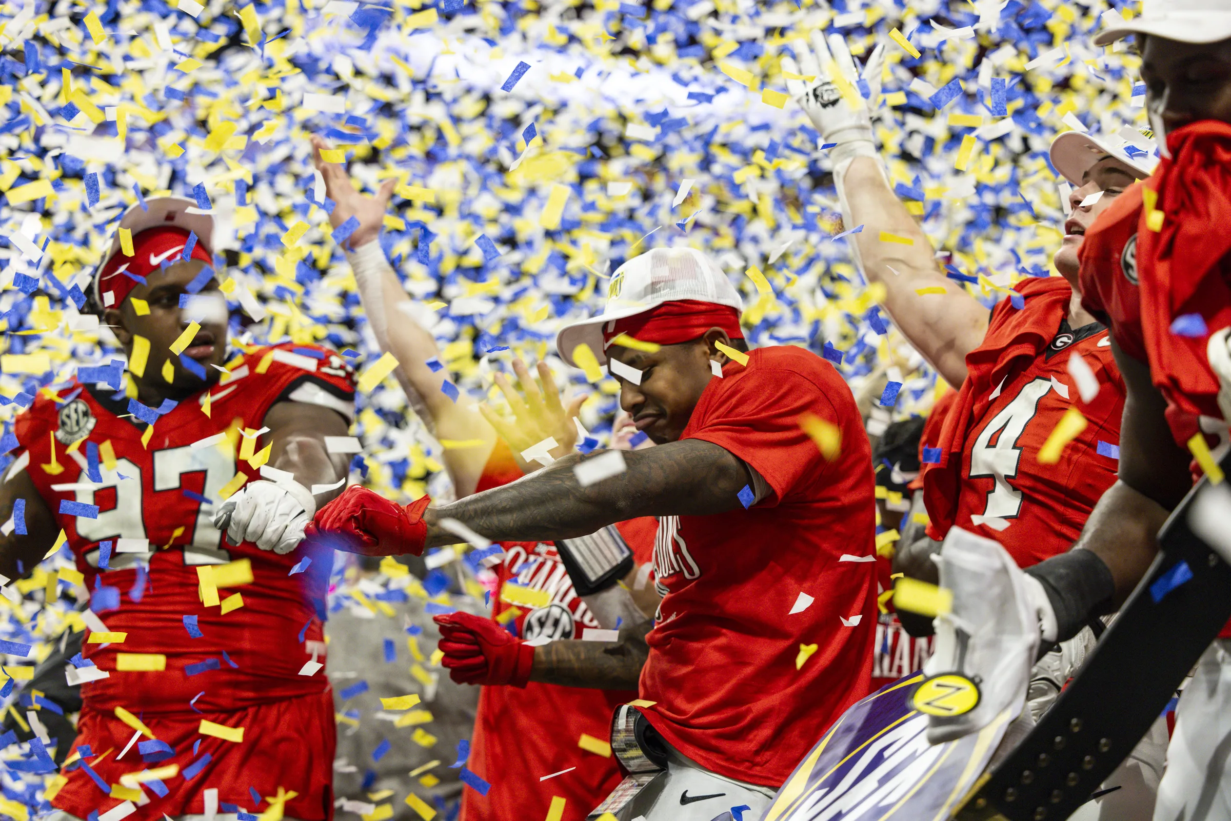Two Georgia football players celebrate their victory in the 2024 SEC Championship game while being showered in yellow and blue confetti on the field.