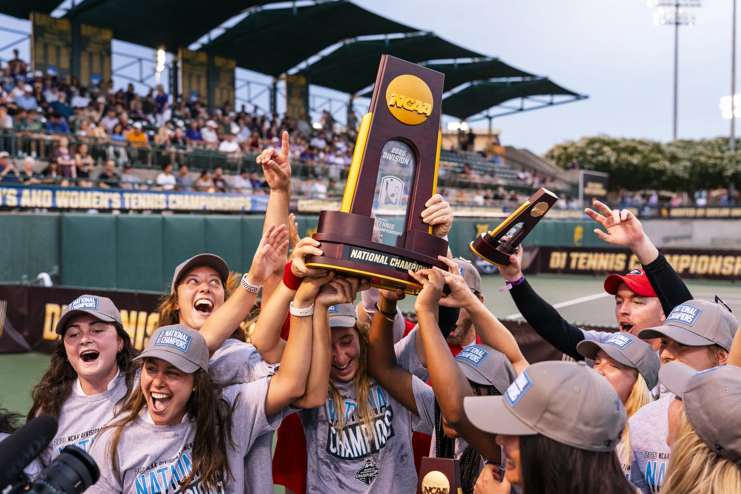 UGA's women's tennis team celebrating their victory together and holding up the NCAA trophy.